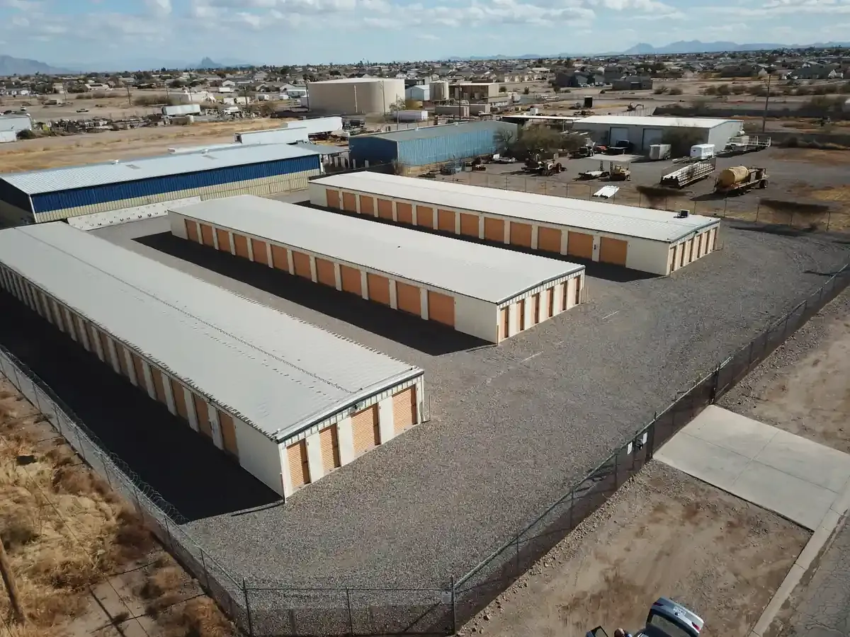 Drone aerial view of a fenced self-storage facility with three long metal storage buildings and gravel drive lanes
